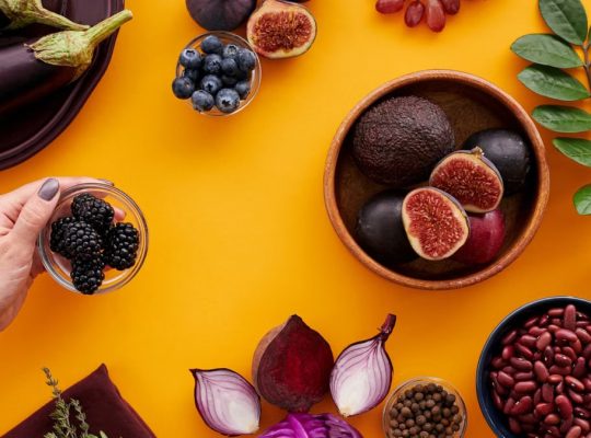 Colorful assortment of fruits and vegetables on a yellow backdrop, highlighting healthy eating.