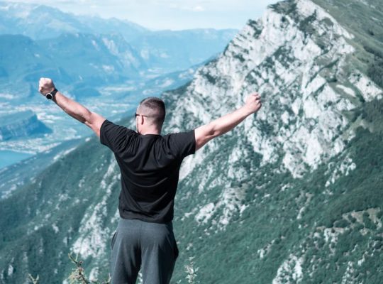 Man standing with arms raised in celebration overlooking a breathtaking mountain landscape.