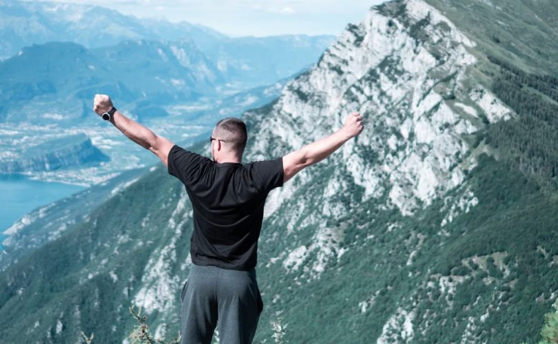 Man standing with arms raised in celebration overlooking a breathtaking mountain landscape.